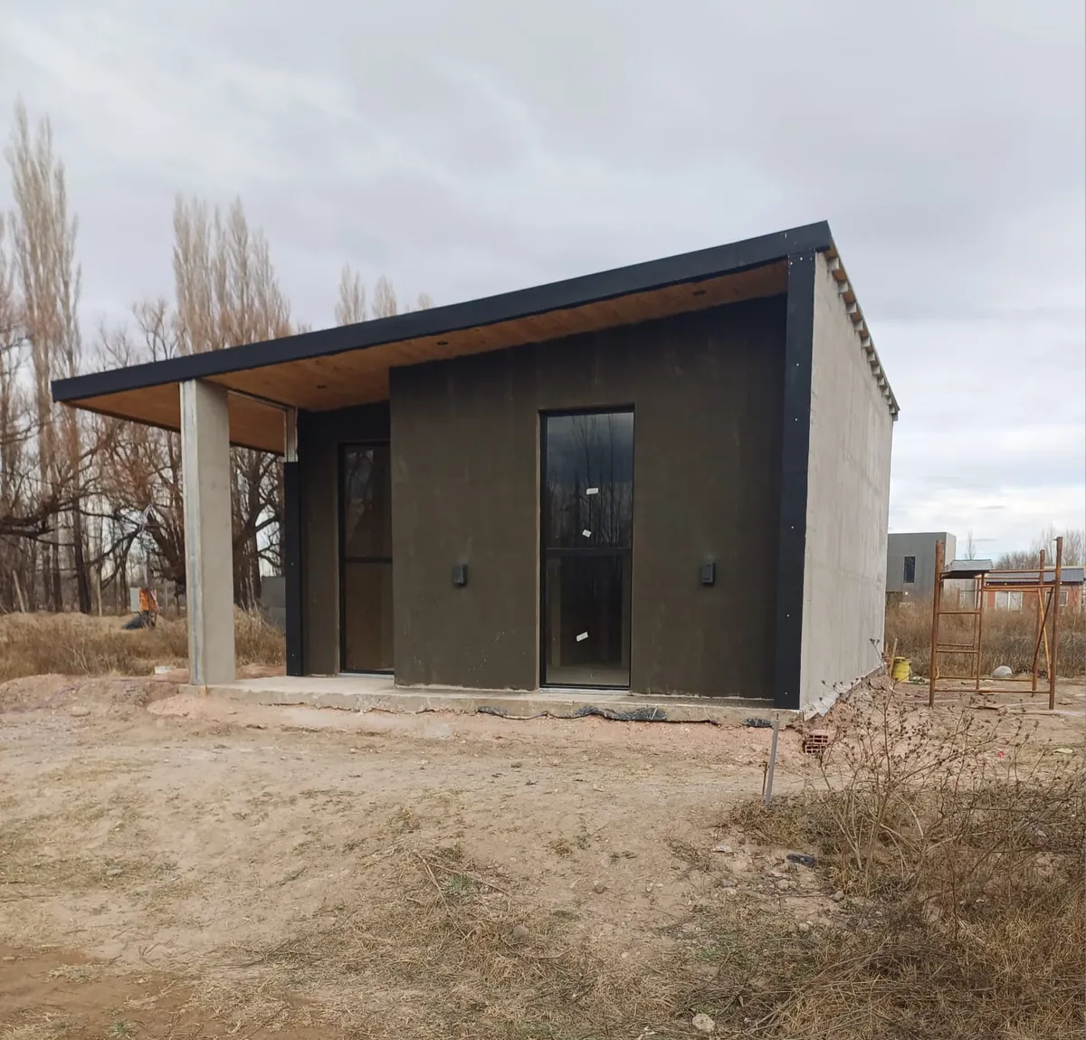 Casa con frente oscuro, techo de madera y aberturas negras