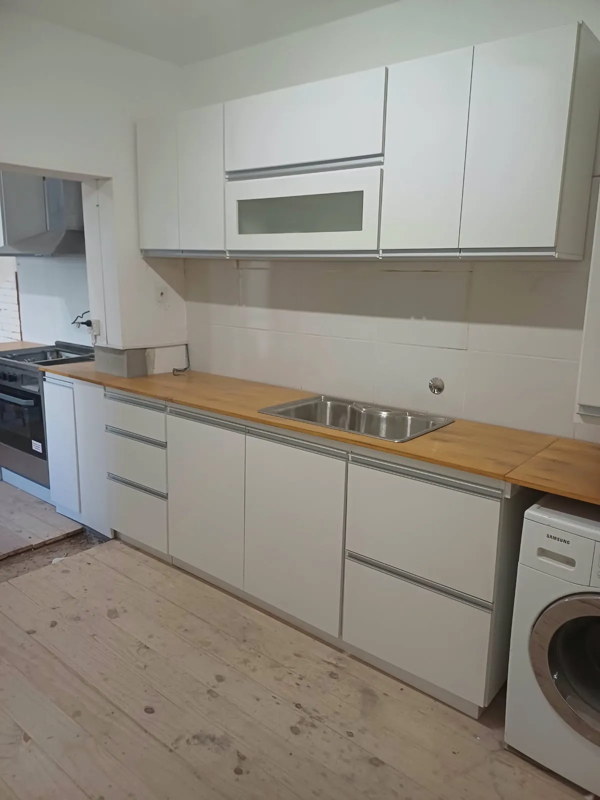 Cocina blanca lineal con tiradores de aluminio y mesada de madera