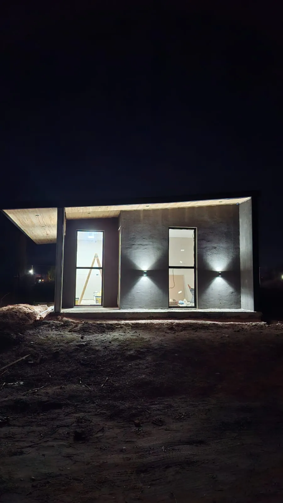 Frente de una casa de noche, con luces en el alero y apliques en la pared
