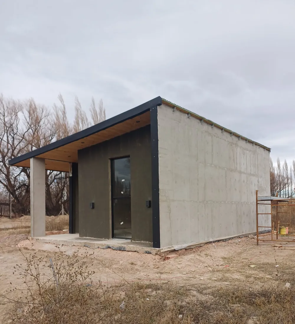 Casa en obra con alero de madera, columna de hormigón y andamio